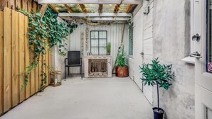 Ein kleiner, umzäunter Patio-Bereich mit Holzlattenzaun, einem schwarzen Korbstuhl, einem kleinen Tisch, einem Kamin und Topfpflanzen.