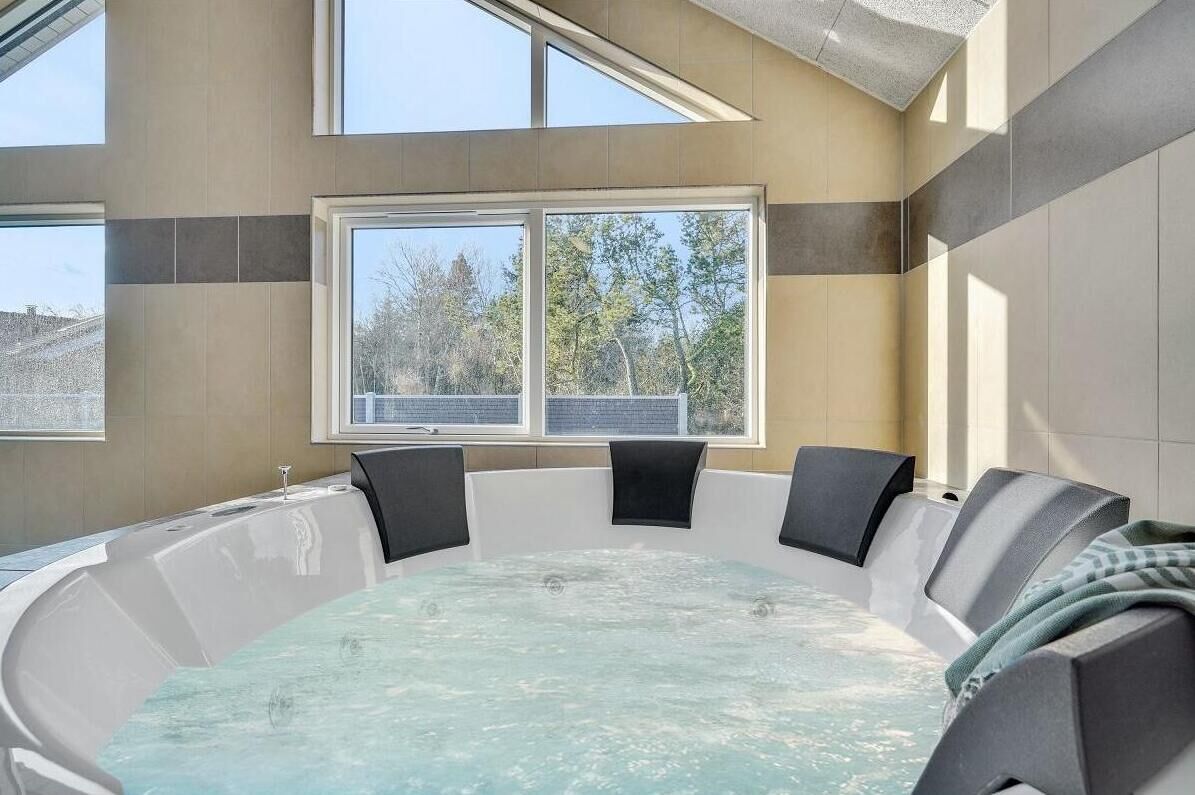 A hot tub with a view of trees through large windows, a skylight, and a modern interior design.