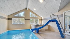 Una piscina interior con un tobogán azul y una escalera, ventanas amplias y un diseño de interiores moderno.