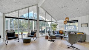 Amplia sala de estar con ventanas grandes, un sofá, sillas y una mesa de centro.