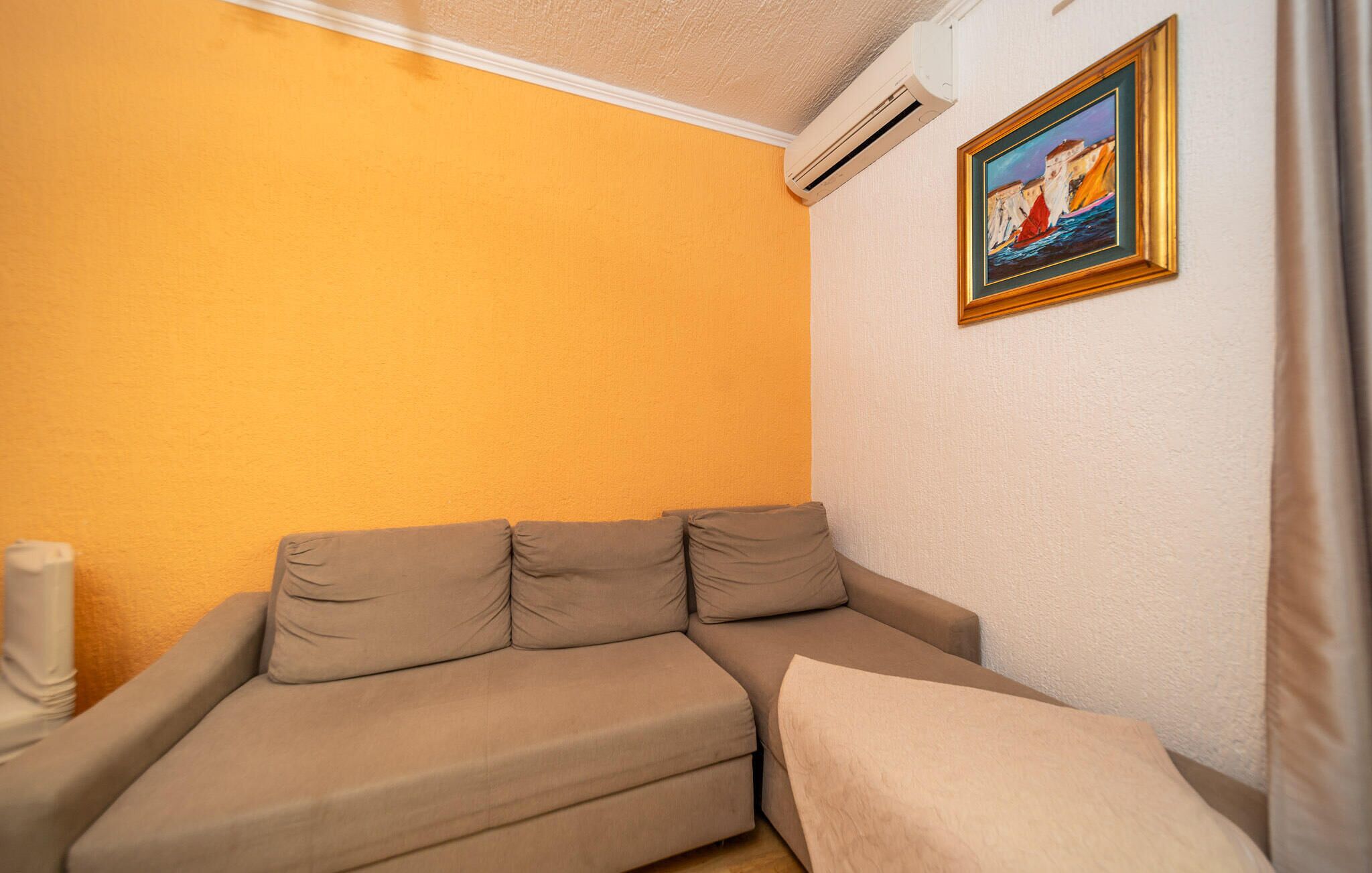 A room with a beige sofa, a painting on the wall, and an air conditioning unit.