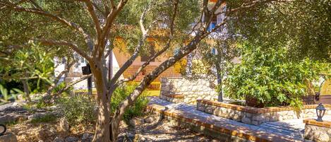 A stone pathway leading to a stone bench area with a view of a building with a yellow facade.