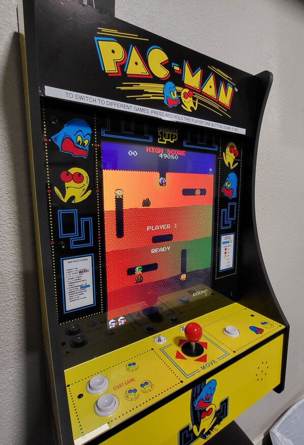 Una máquina de arcade Pac-Man con diseño amarillo y negro, que incluye un joystick y botones en la parte frontal.