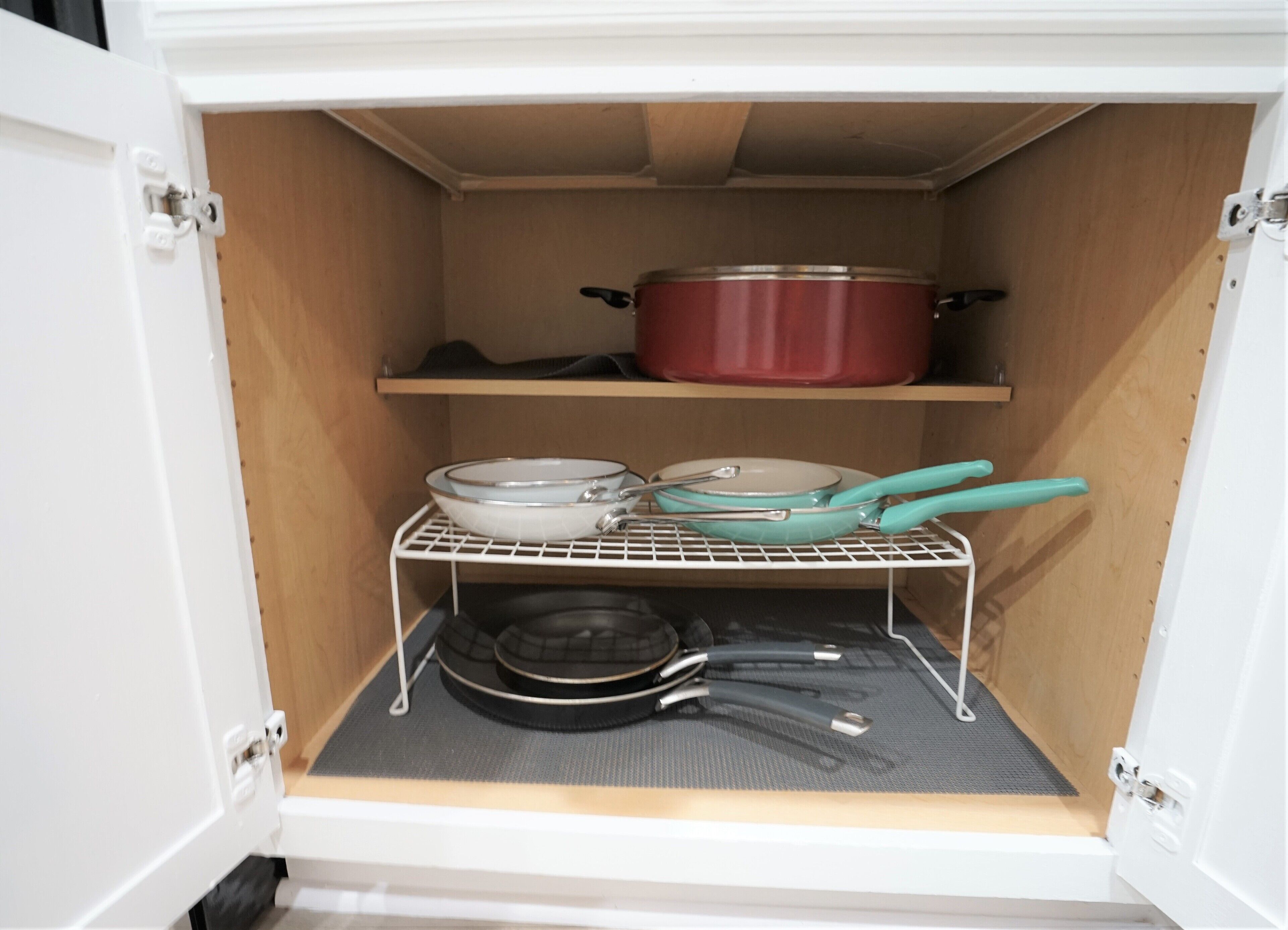 A kitchen cabinet with shelves holding cookware and a pot.