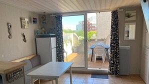 En kompakt opholdsstue med et tekøkken, et spiseområde og en skydedør til en udendørs terrasse.
