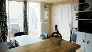 Et hyggeligt rum med et træbord, en flaske og en stol. En dør fører til en balkon, og der er et ur på væggen.