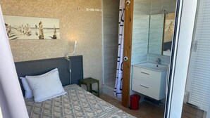 Et soveværelse med et sengetæppe med mønster, et natbord, en lille skammel og en rød skraldespand.