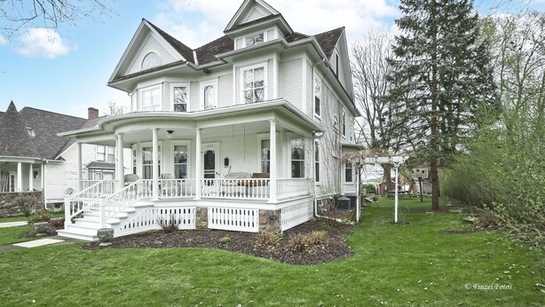 Une grande maison à deux étages, dotée d’une véranda qui fait le tour de la maison et de fondations en pierre.