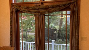 Une pièce dotée d’une grande fenêtre à cadre en bois, d’un banc en bois et offrant une vue sur une terrasse et un jardin.