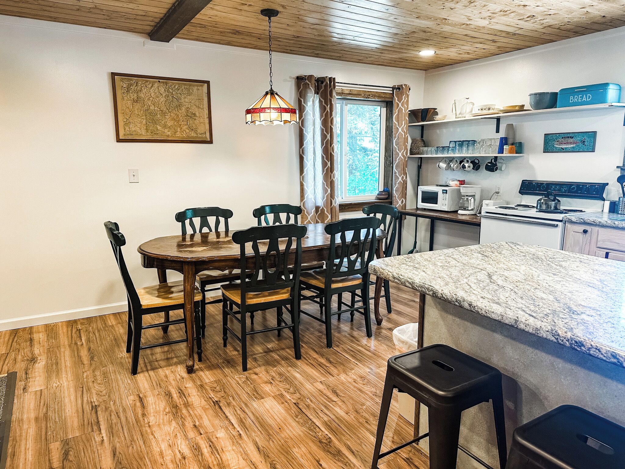 A dining area with a wooden table and chairs, a kitchen with appliances, and a window with curtains.