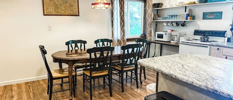 A dining area with a wooden table and chairs, a kitchen with appliances, and a window with curtains.