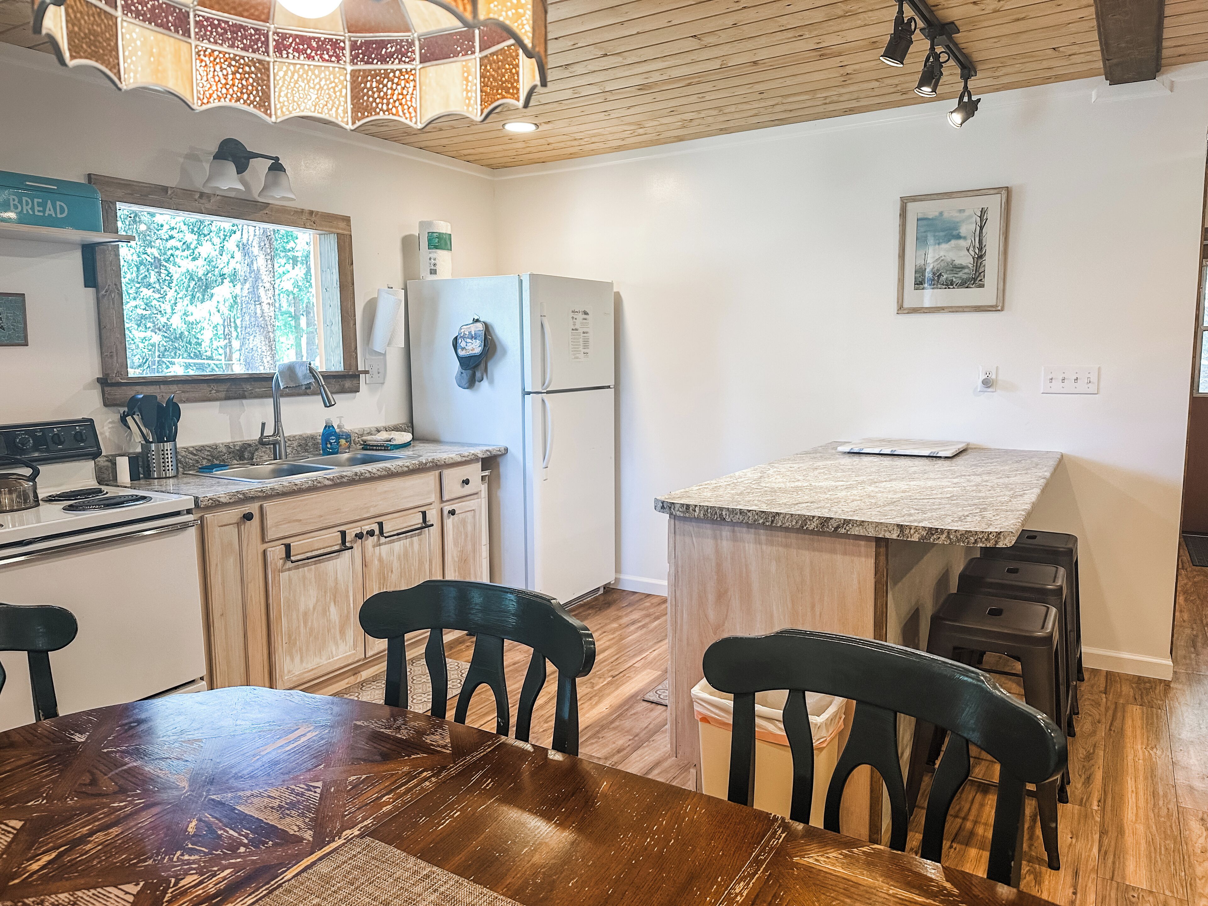 A kitchen with wooden cabinets, a stove, a sink, and a dining area with a wooden table and chairs.