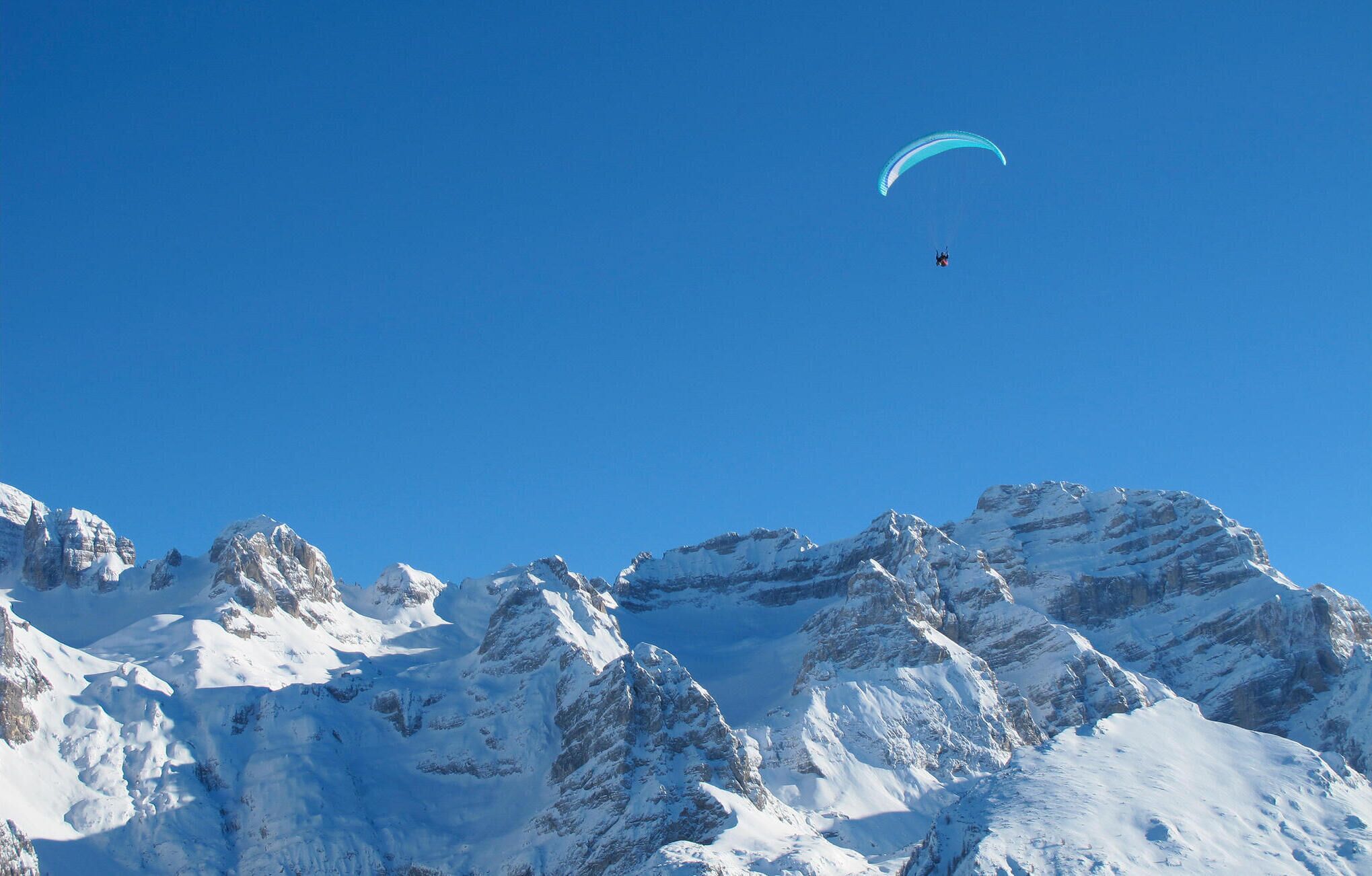 Paisagem montanhosa coberta de neve com um parapente no céu.