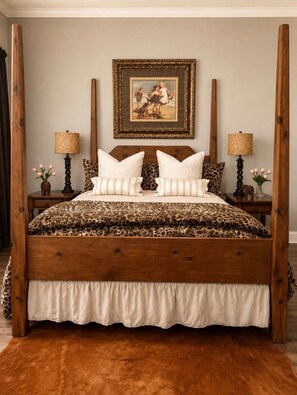 A four-poster bed with a leopard print bedspread, two nightstands with lamps, a framed picture above the bed, and a brown rug on the floor.