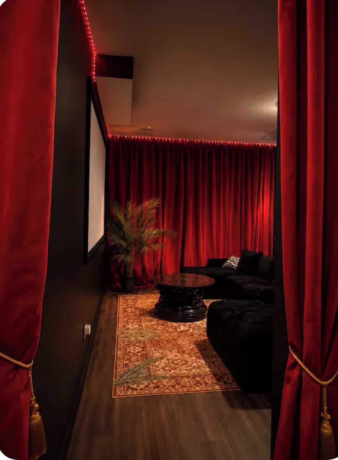 A room with a dark wooden floor, a black sofa, a round coffee table, and a red curtain.