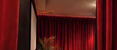 A room with a dark wooden floor, a black sofa, a round coffee table, and a red curtain.