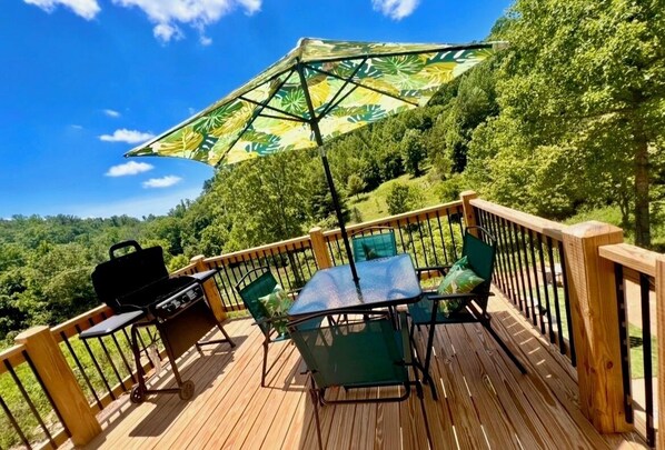 A wooden deck with a table and chairs, a grill, and a large umbrella providing shade.