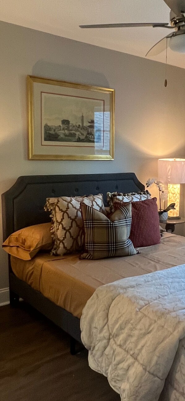 A bedroom with a bed, pillows, a framed picture on the wall, and a lamp on a bedside table.