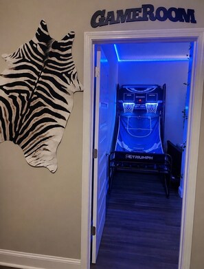 A room with a gaming area featuring a Triumph gaming machine, a zebra-patterned wall decoration, and a sign labeled 'GAME ROOM'.