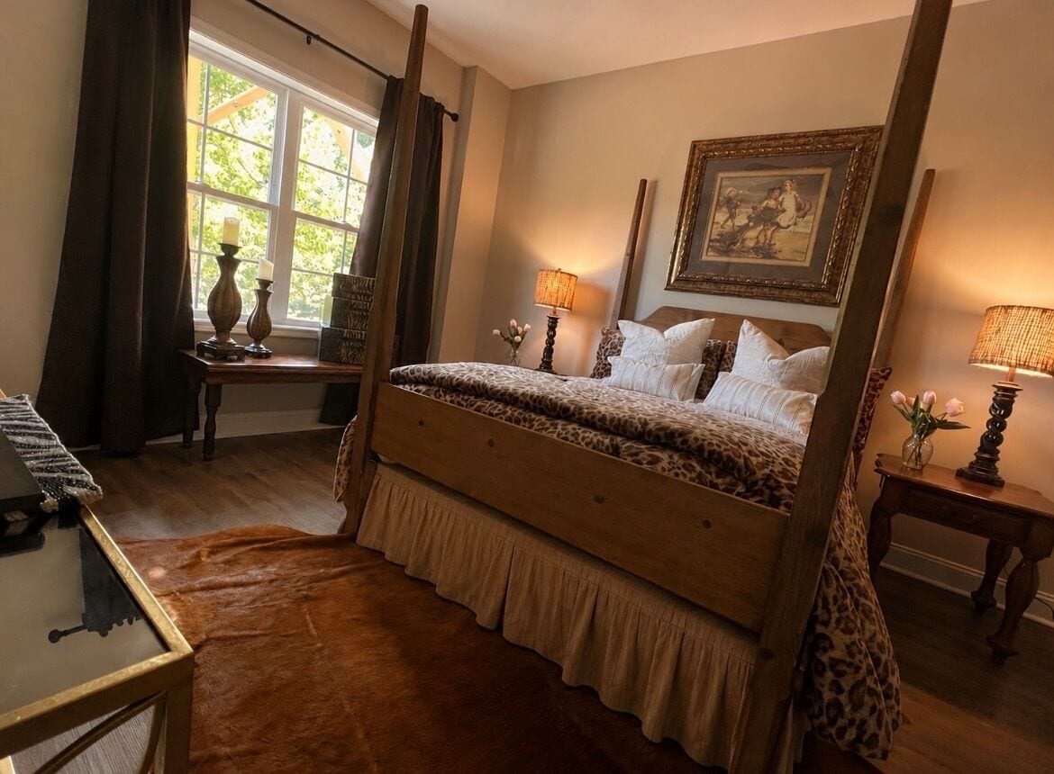 A bedroom with a four-poster bed, a wooden desk, a lamp, and a framed picture on the wall.