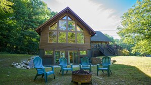 Eine Blockhütte mit großem Panoramafenster, einer Terrasse mit Stühlen und einer Feuerstelle.