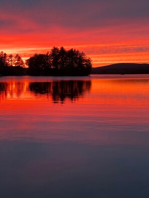 A serene lakeside view at sunset with a forested island reflected in calm waters.