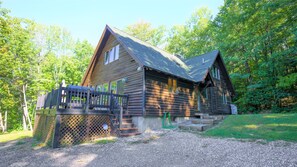 A log cabin with a wooden deck and a gravel driveway.