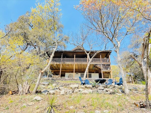 A two-story wooden cabin with a balcony, surrounded by trees and rocks.