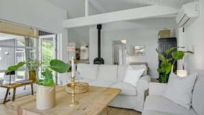 A modern living room with a white sofa, a wooden coffee table, and large green plants. - 4 bedroom lovely home in Gilleleje (Gilleleje)