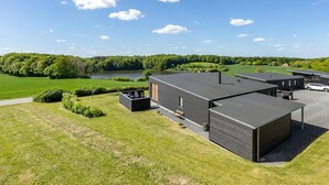 A modern building with a flat roof, surrounded by a well-maintained lawn and a lake. - 3 bedroom awesome home in Aabenraa (Aabenraa)