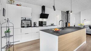 A modern kitchen with white cabinetry, a black island, a built-in oven, a coffee maker, and a black stove. - 3 bedroom awesome home in Aabenraa (Aabenraa)