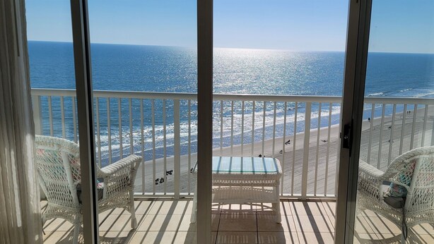 A balcony with wicker chairs and a glass table overlooking a beach with waves and a clear sky. - Oceanfront 3 Bedroom/2Bath SeaWatch Resort (Myrtle Beach)