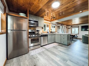 A modern kitchen with stainless steel appliances, wooden ceiling, and a dining area with a view.