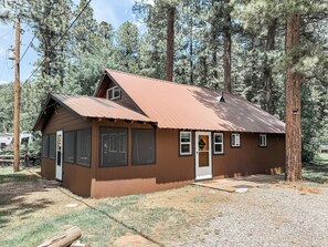 Une petite cabane à un seul étage, avec un toit en métal, entourée de grands pins.