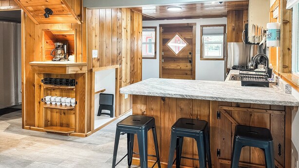 A kitchen with wooden cabinets, a coffee machine, and bar stools. - Croll Cabins-Martin Lakeside (#2) at Vallecito Lake (Bayfield)