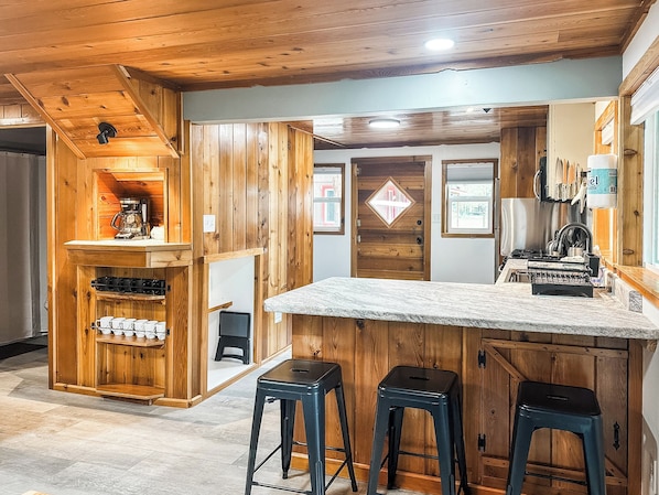 A kitchen with wooden cabinets, a coffee machine, and bar stools. - Croll Cabins-Martin Lakeside (#2) at Vallecito Lake (Bayfield)