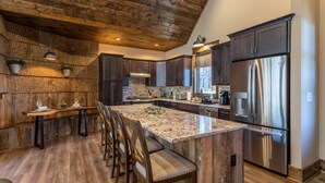 A modern kitchen with dark wood cabinets, a large island with bar stools, stainless steel appliances, and a rustic ceiling. - Stillness Springs at Eagles Nest - Pet Friendly, Two master suites, firepit, hot tub, creek, 1 acre! (Banner Elk)