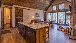 A spacious kitchen with a large island, wooden ceiling beams, and large windows offering views of the outdoors. - Stillness Springs at Eagles Nest - Pet Friendly, Two master suites, firepit, hot tub, creek, 1 acre! (Banner Elk)