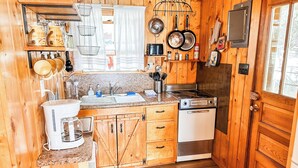 Une cuisine compacte avec des meubles de rangement en bois, une cuisinière, un évier et un petit réfrigérateur.