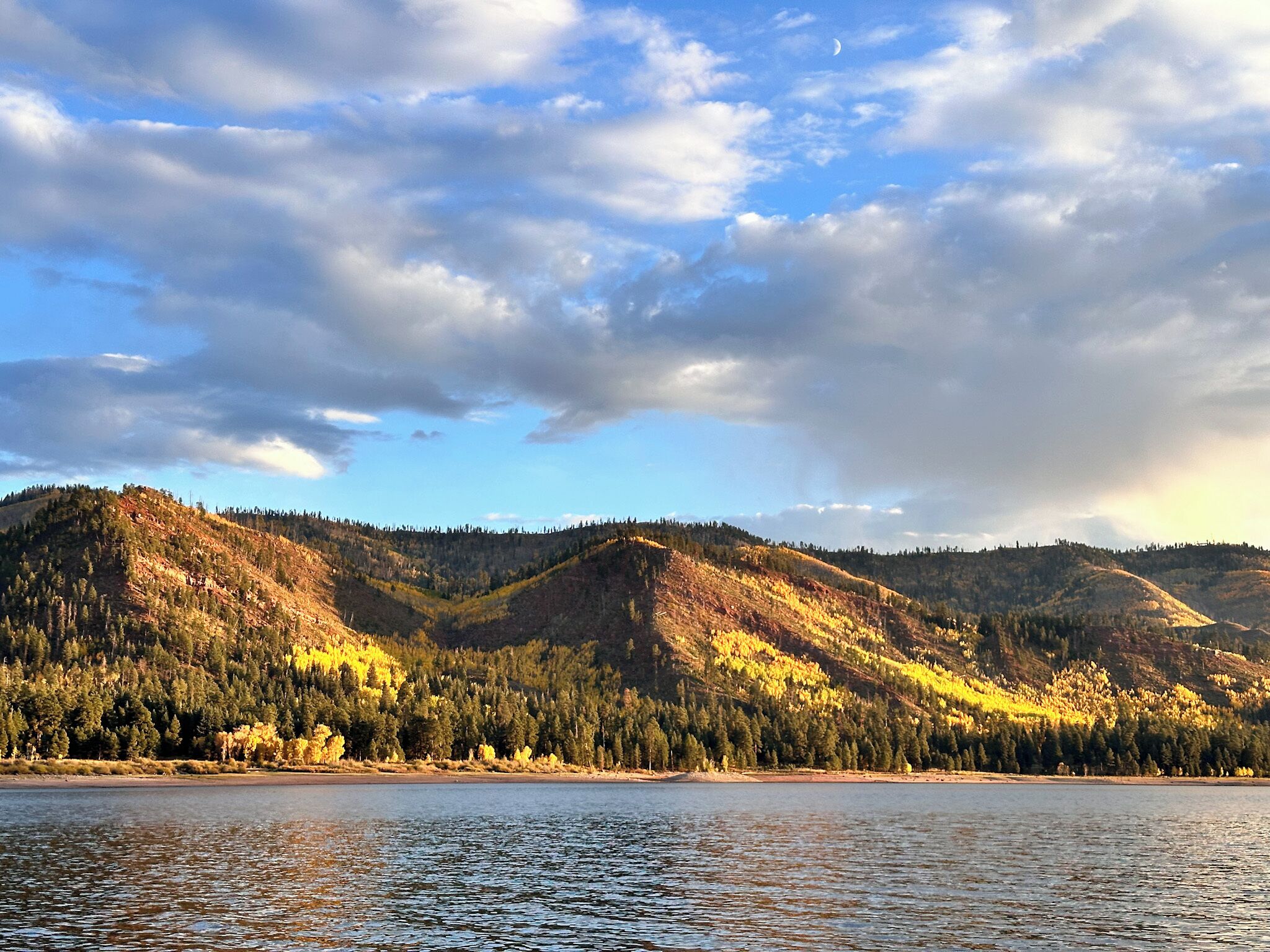Un lac entouré de collines boisées, sous un ciel dégagé.