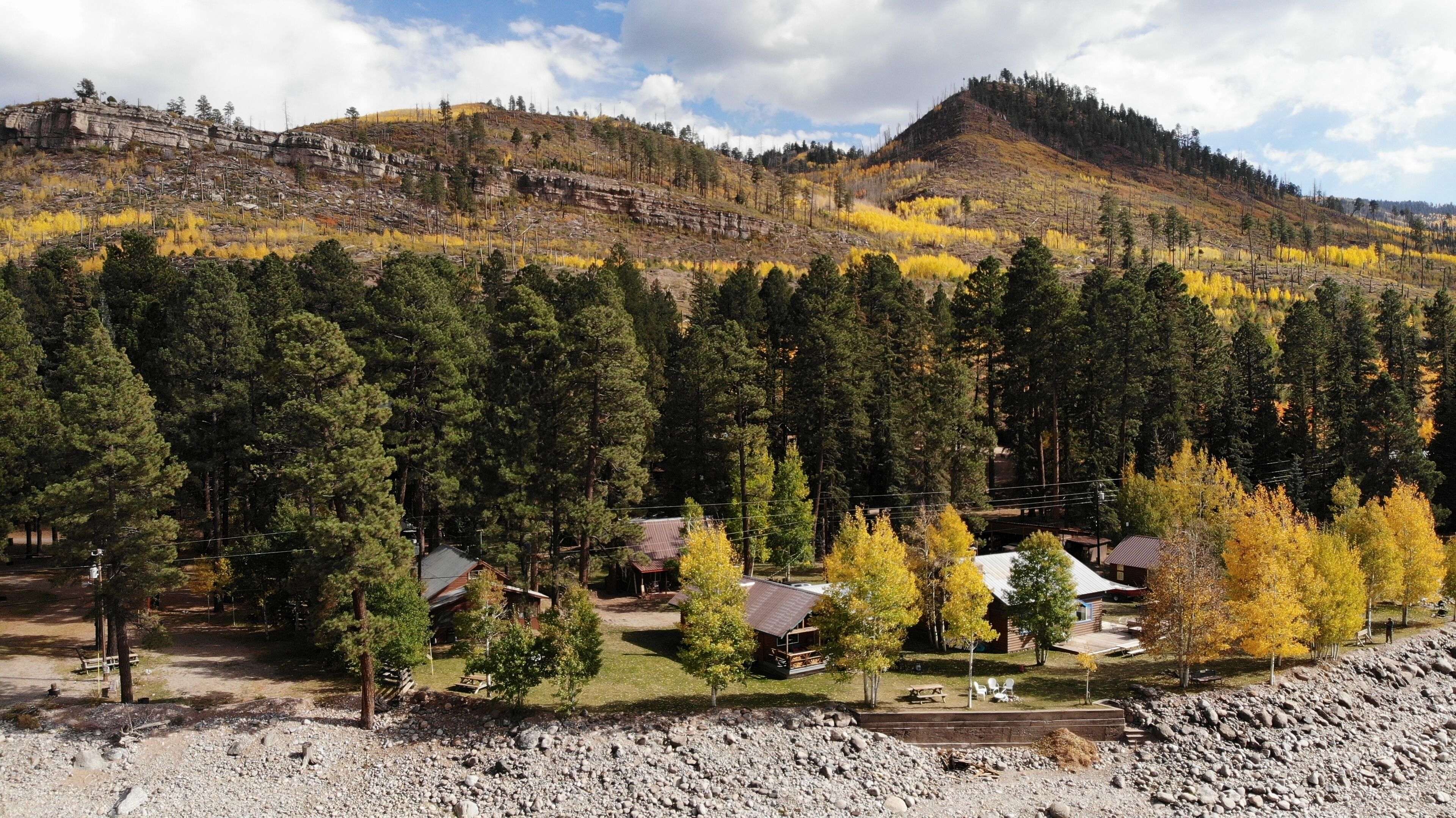 A mountainous area with a forest, a small cabin, and a rocky foreground.
