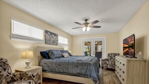 Um quarto com uma cama, mesa de cabeceira, poltrona, cômoda e ventilador de teto.