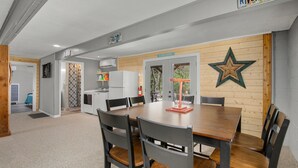 Uma sala de jantar com mesa e cadeiras de madeira, uma cozinha ao fundo e uma decoração em forma de estrela na parede.