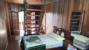 Une pièce en bois avec un lit, une chaise et une petite table. Un escalier mène à un niveau supérieur.
