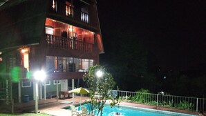 Vue nocturne d’un immeuble à deux étages avec une piscine.