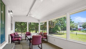 A sunroom with large windows, a ceiling fan, and several purple chairs.