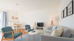A modern living room with a sofa, chairs, a coffee table, a TV, and a dining area with a table and chairs. - Friesennerz - Hedighuis - Friesennerz (Sylt)