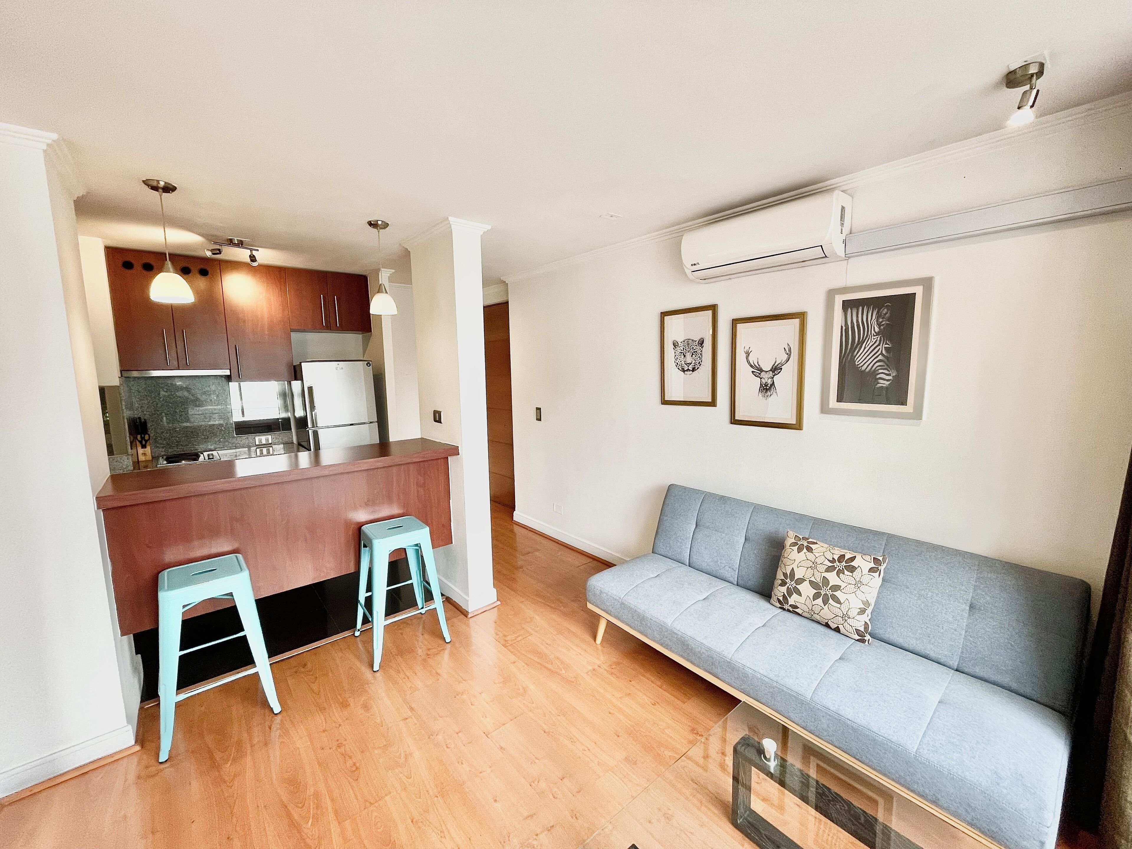 A compact living space with a kitchenette, a sofa, and a dining area with stools.