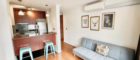 A compact living space with a kitchenette, a sofa, and a dining area with stools.