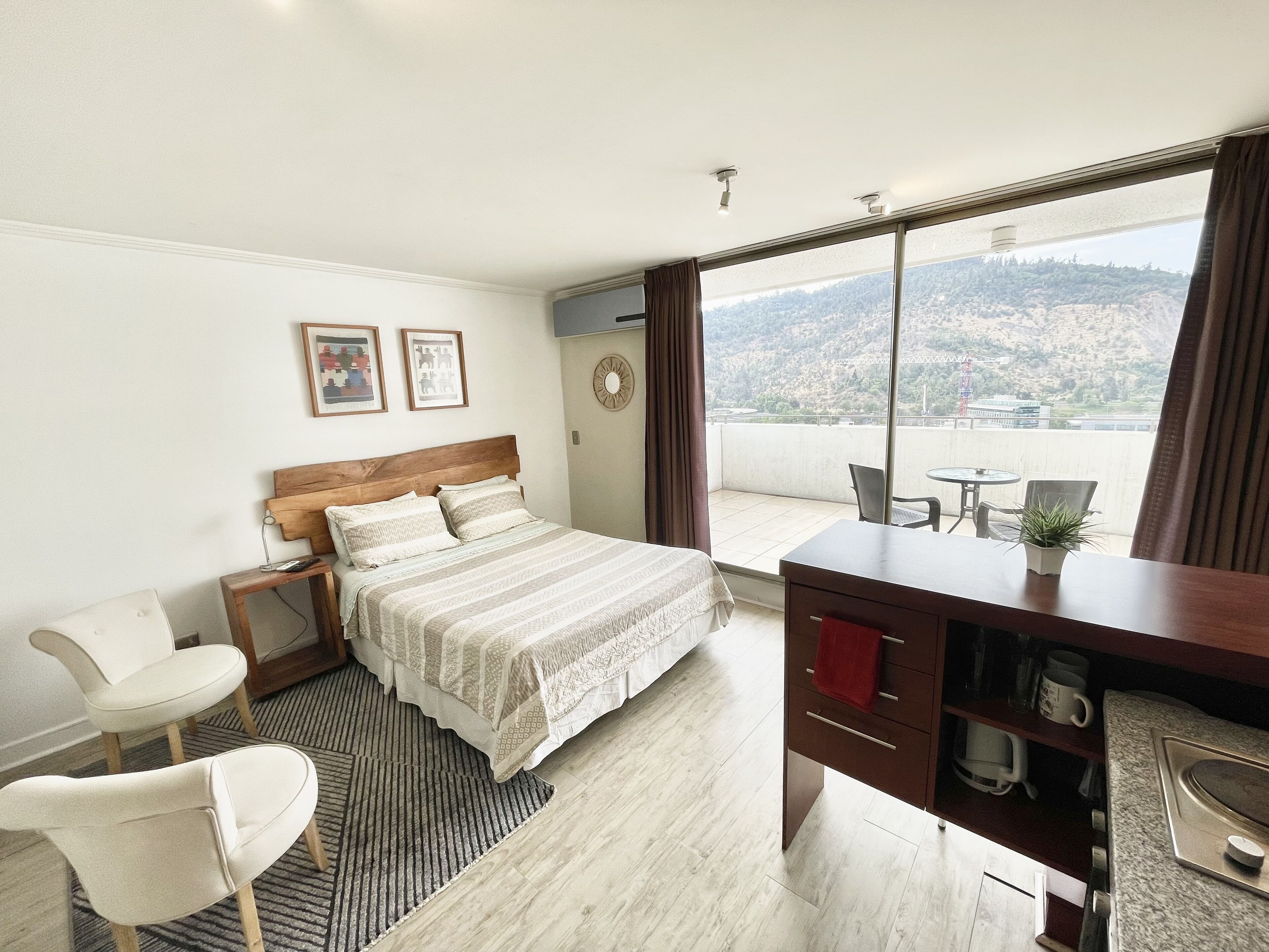 Ein Hotelzimmer mit Bett, Schreibtisch, Stuhl, kleinem Tisch und Blick auf eine Stadtkulisse durch große Fenster.
